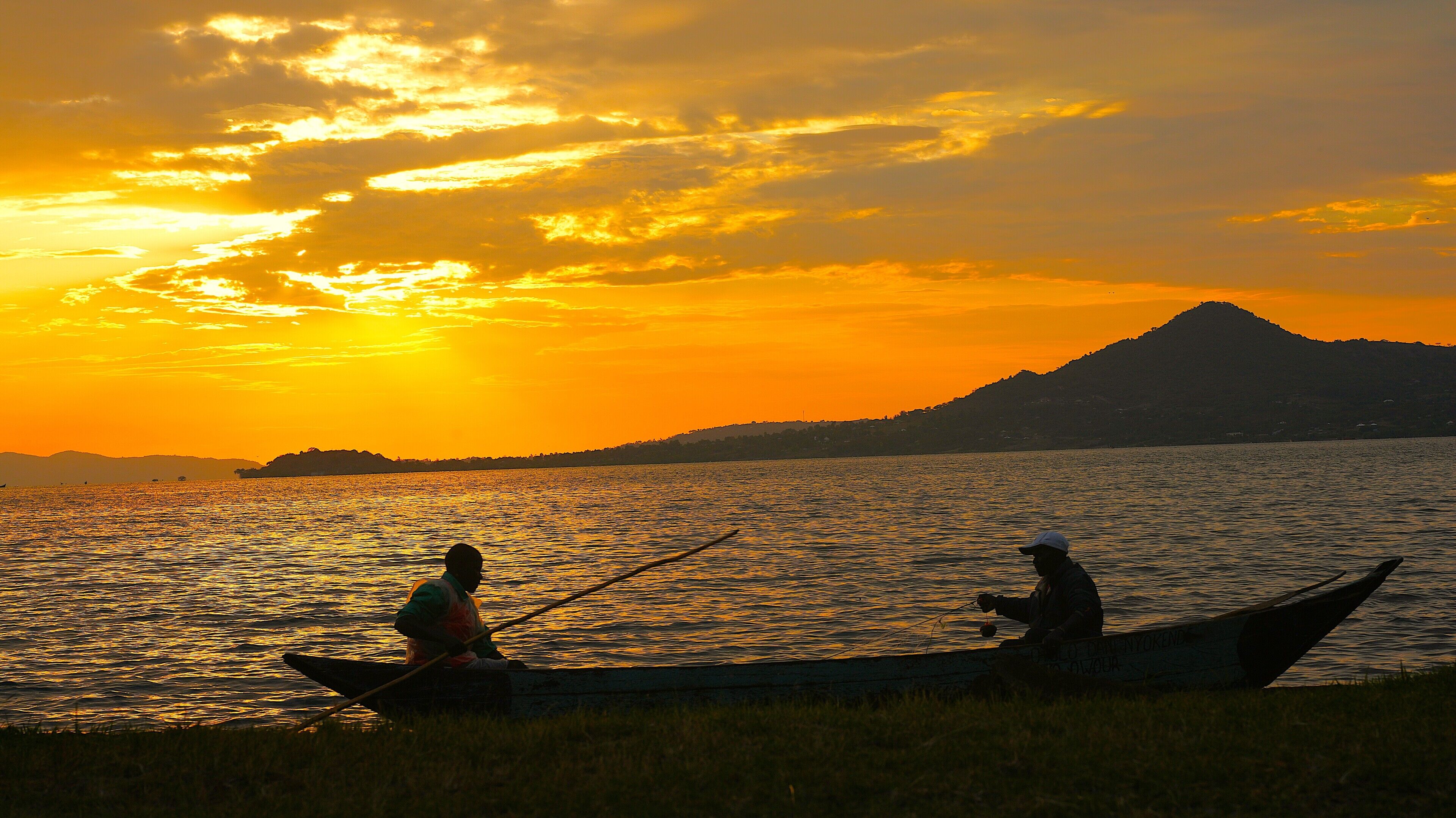 Two people in a boat on a calm body of water during sunset.