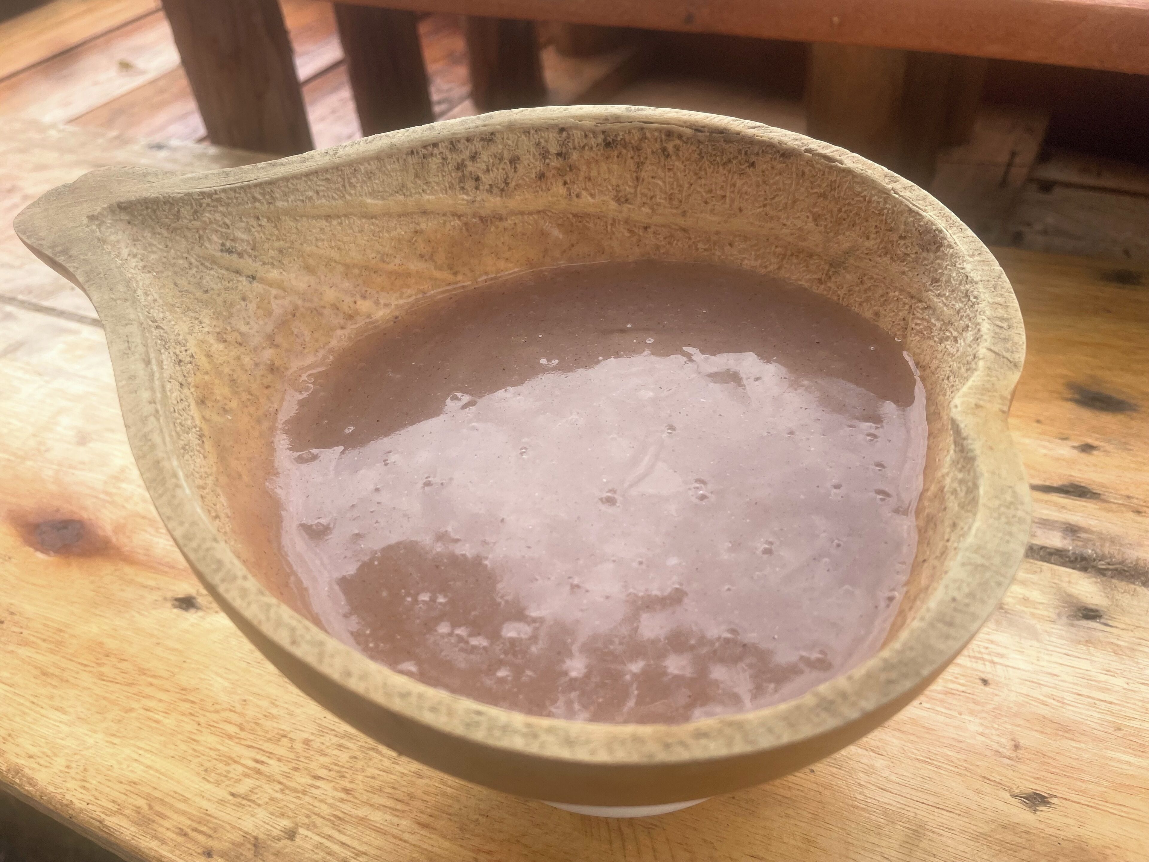 A rustic ceramic bowl filled with a brown liquid, placed on a wooden surface.