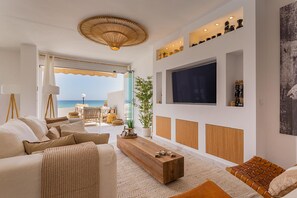 A modern living room with a large TV, comfortable seating, a wooden coffee table, and a view of the sea. - 3128 Beachfront Casa Luna in Aldea Beach (Manilva)
