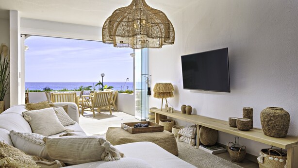 Een moderne woonkamer met een grote bank, een aan de muur bevestigde televisie en uitzicht op de oceaan.