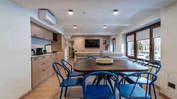 A modern kitchen with built-in appliances, a dining area with a wooden table and blue chairs, and a large window with a view of the street.