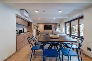 Una cocina moderna con electrodomésticos integrados, un comedor con mesa de madera y sillas azules, y un ventanal con vistas a la calle.