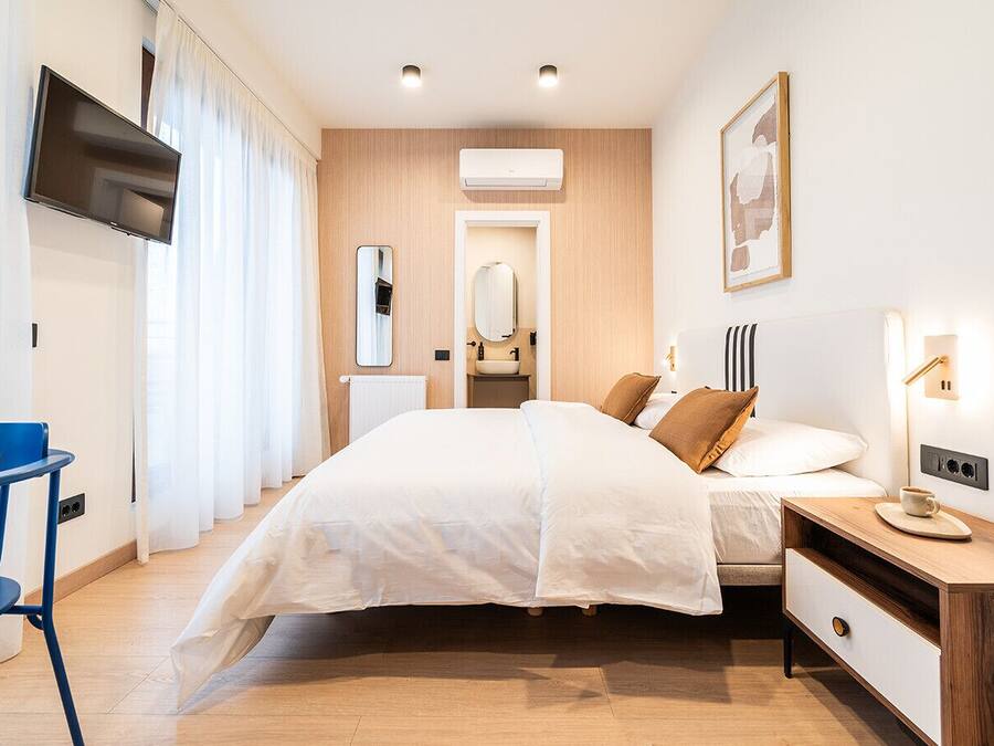 Une chambre à coucher moderne avec un lit, une table de chevet et un téléviseur fixé au mur.