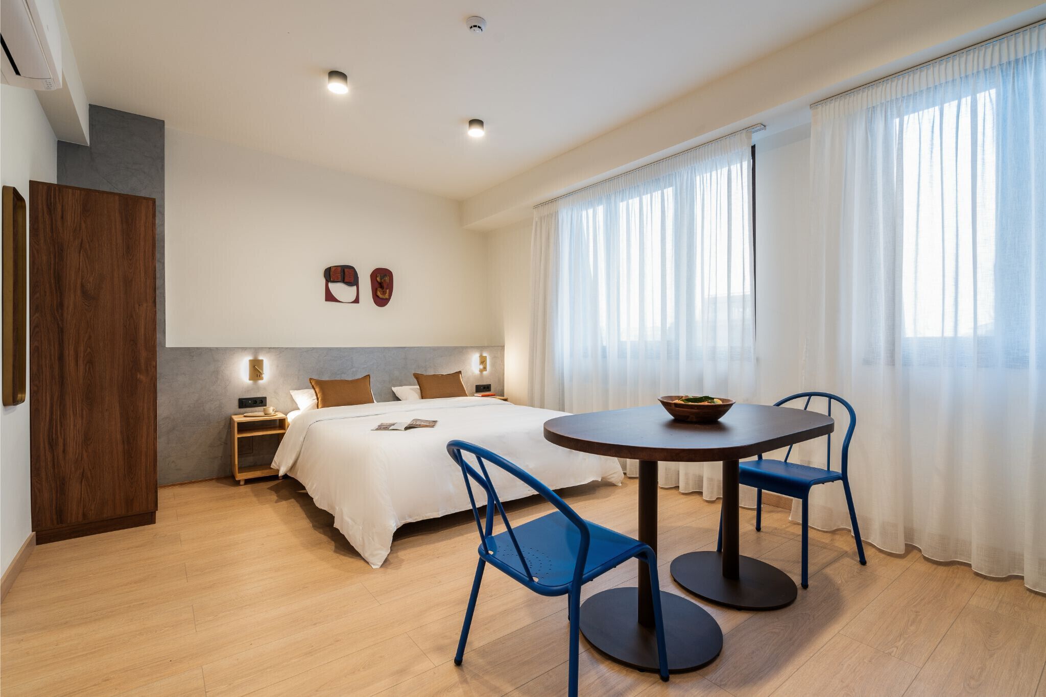A modern hotel room with a bed, bedside table, lamp, and a round table with chairs.
