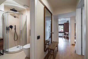 Un baño moderno con ducha de vidrio, inodoro y banco de madera en un pasillo.