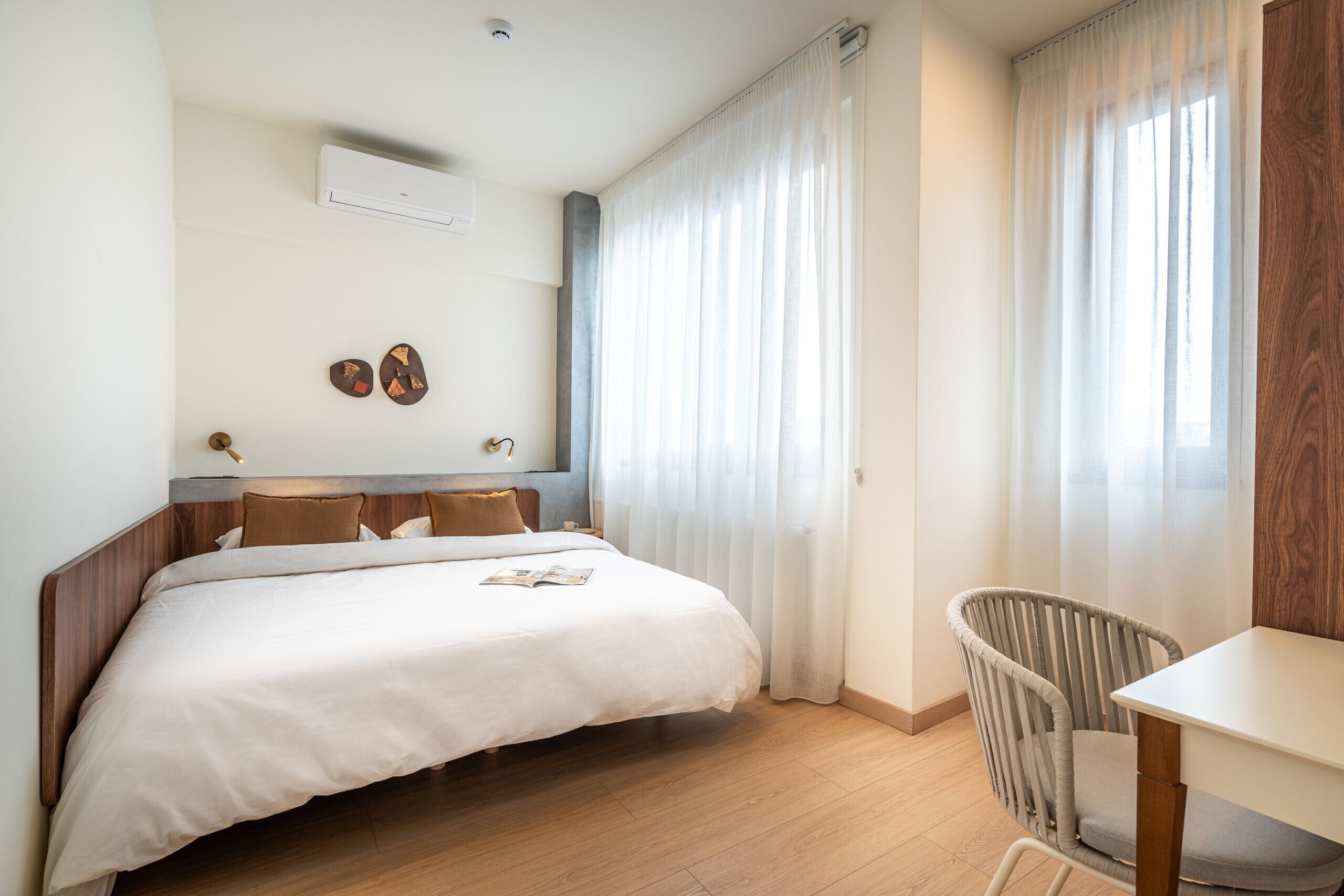 Een hotelkamer met een bed, een stoel, een tafel en een raam met gordijnen.