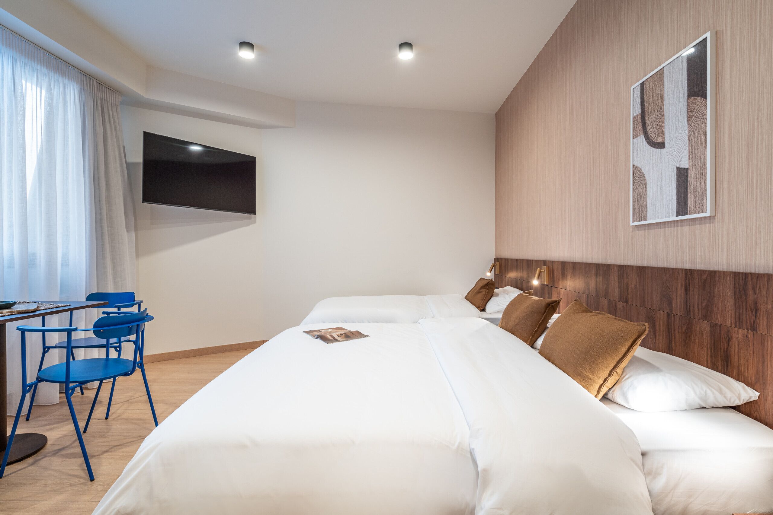 A hotel room with a large bed, a desk with chairs, a flat-screen TV, and a wooden headboard.