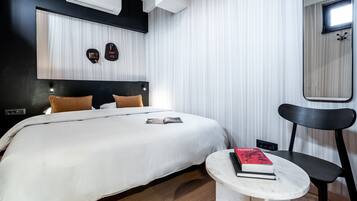 A modern hotel room with a large bed, a small table with a book, a chair, and a mirror.