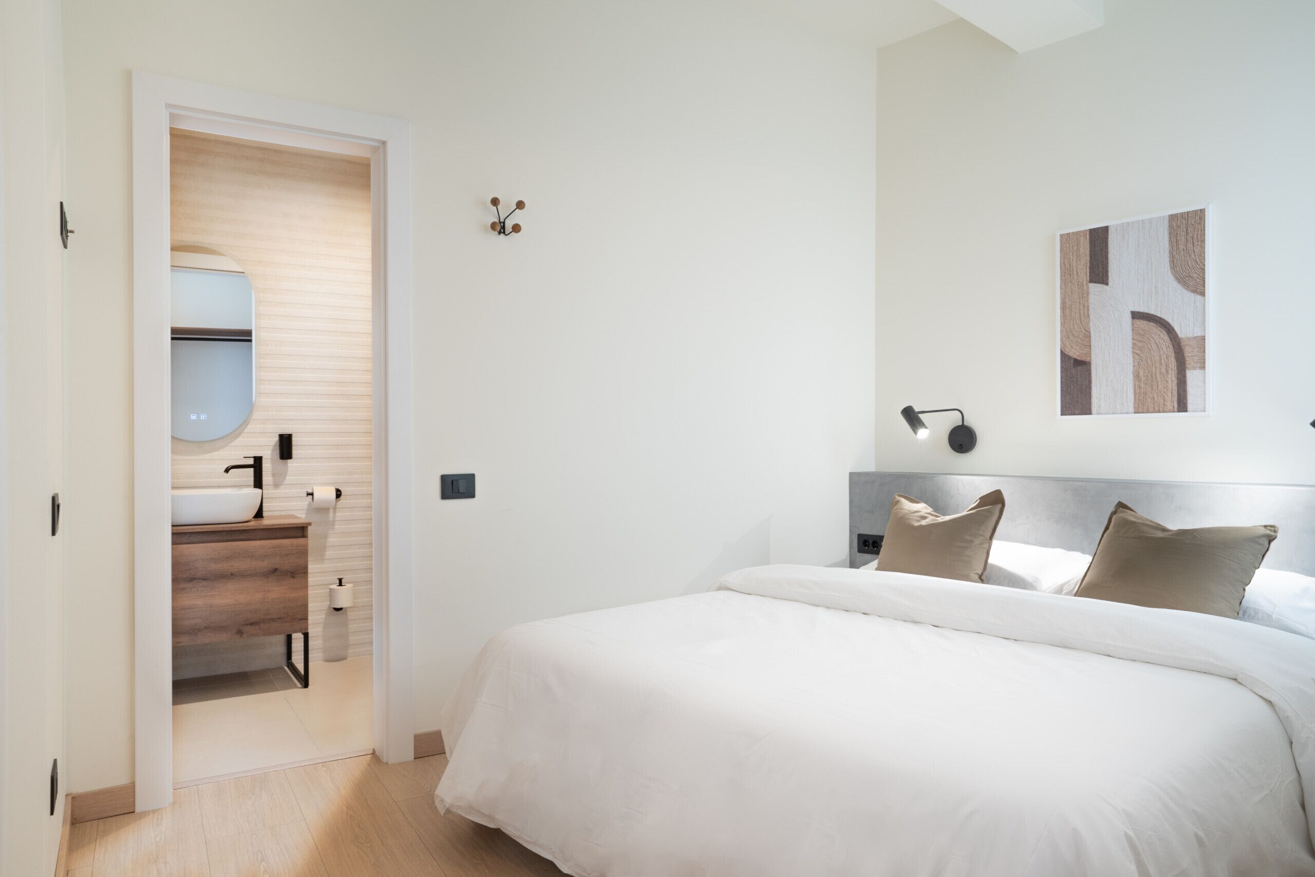 Une chambre à coucher avec un lit, une table de chevet, une lampe fixée au mur et un tableau.
