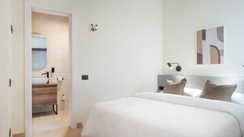 Une chambre à coucher avec un lit, une table de chevet, une lampe fixée au mur et un tableau.