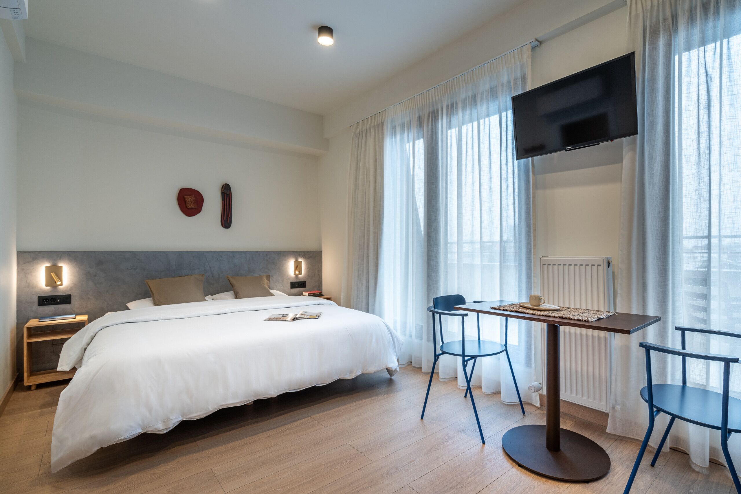 Una habitación de hotel moderna con una cama grande, mesitas de noche, un televisor de pantalla plana y un comedor con sillas.