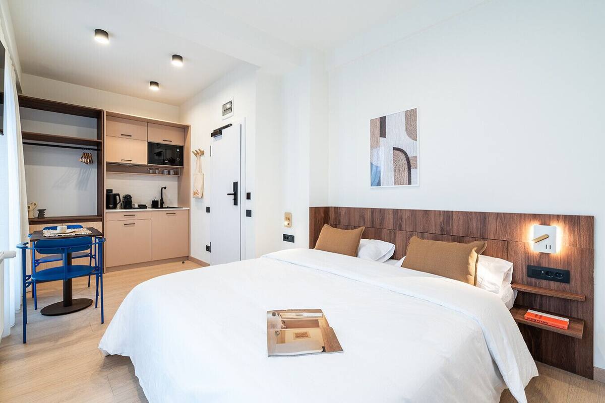 A hotel room with a large bed, a desk with a chair, a kitchenette, and a bathroom.