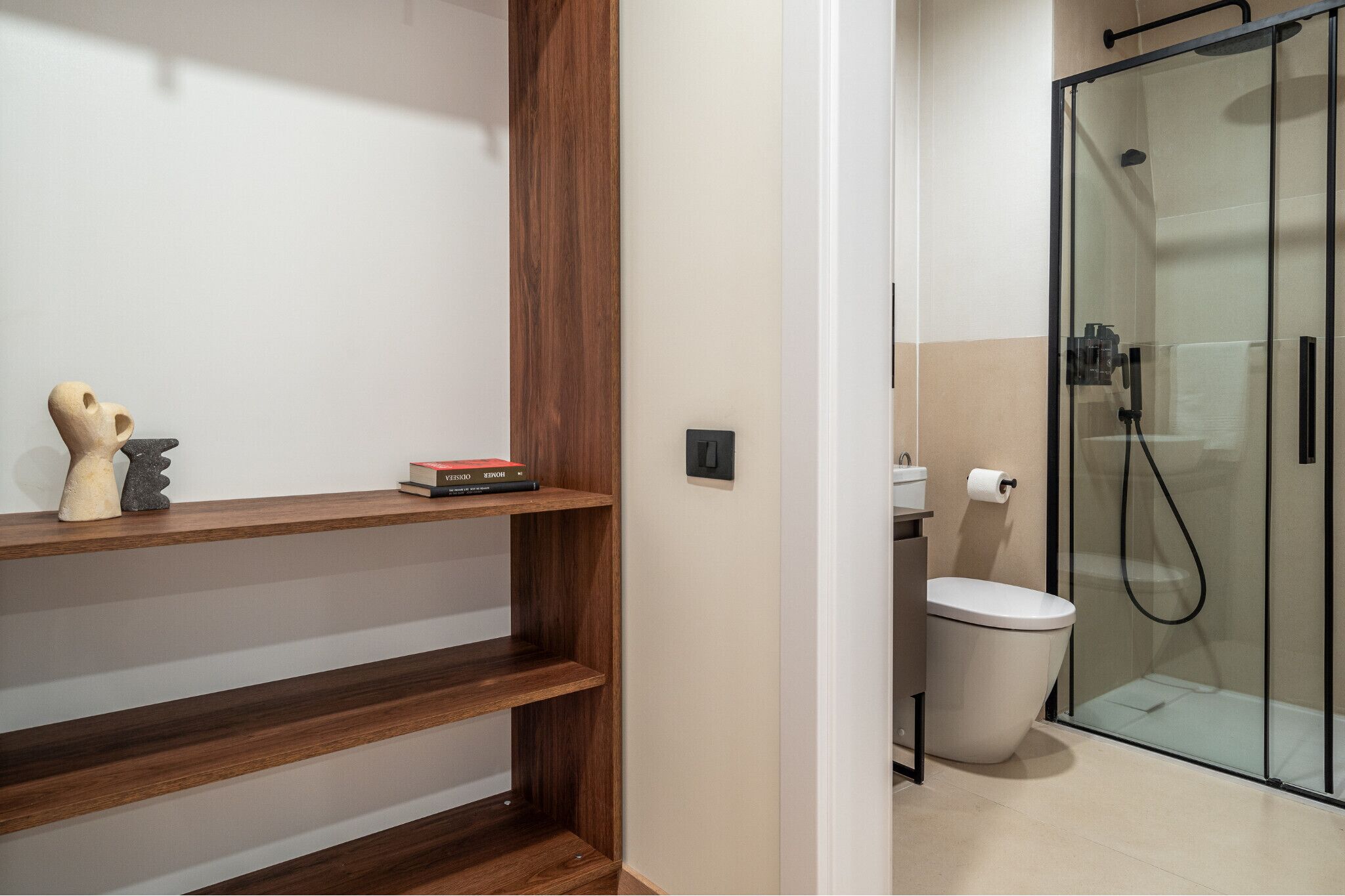 Un baño moderno con ducha de vidrio, inodoro y estantes de madera con objetos decorativos.