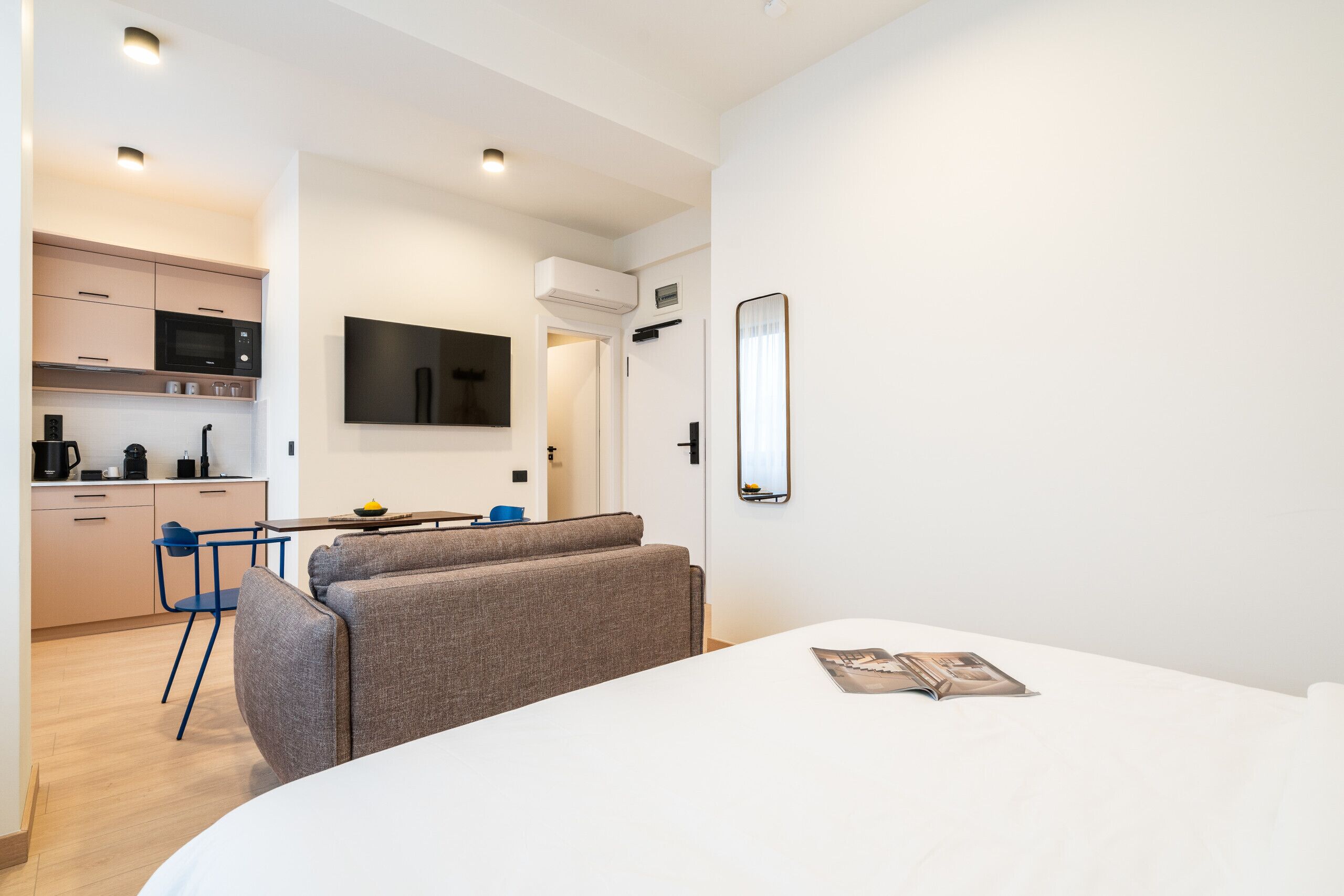 Een moderne hotelkamer met een bed, een kleine kitchenette, een zithoek met een bank en stoelen, en een aan de muur bevestigde televisie.