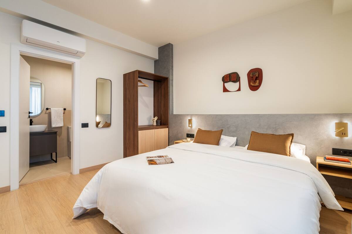 A modern hotel room with a large bed, a walk-in closet, a bathroom with a sink and mirror, and a wall-mounted shoe rack.