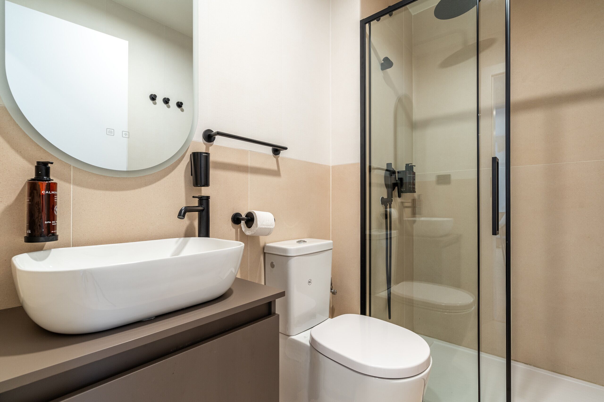 Un baño moderno con un lavamanos de diseño, un inodoro y una ducha con mampara de vidrio.