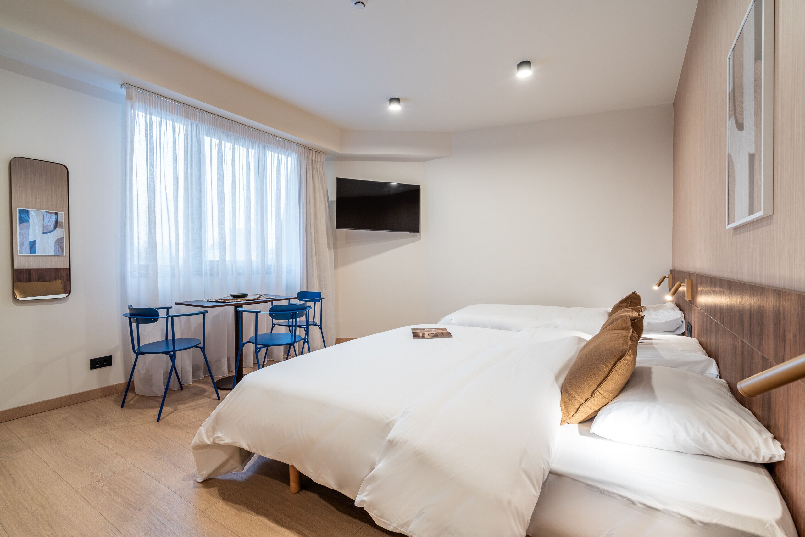 Une chambre d’hôtel avec un grand lit, un bureau avec des chaises, un téléviseur fixé au mur et une fenêtre avec des rideaux.