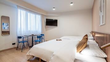 Une chambre d’hôtel avec un grand lit, un bureau avec des chaises, un téléviseur fixé au mur et une fenêtre avec des rideaux.