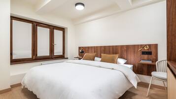 A bedroom with a large bed, wooden headboard, a nightstand, a chair, and a window with frosted glass.