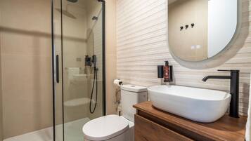 Un baño moderno con ducha de vidrio, inodoro blanco y tocador de madera con lavamanos blanco.