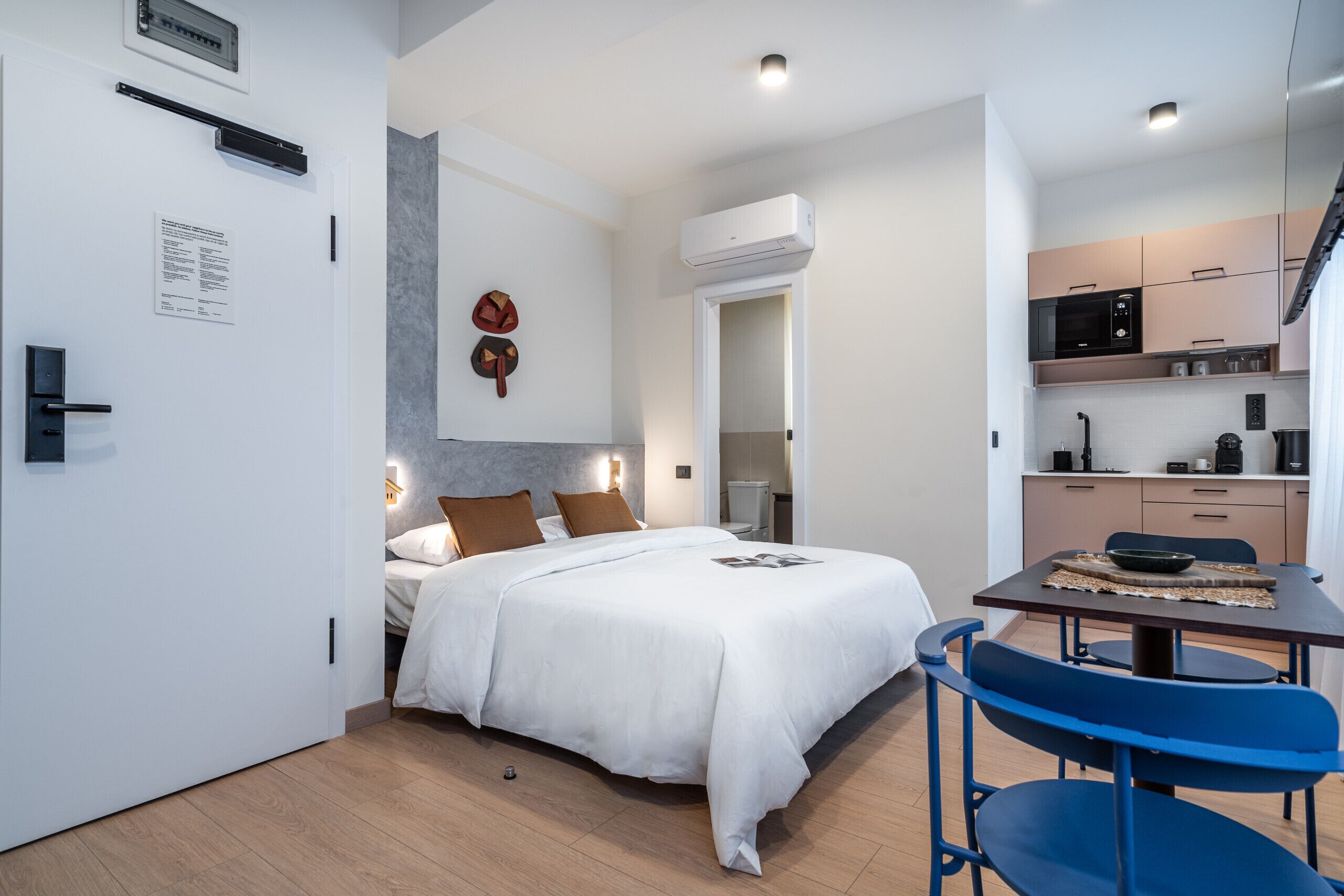 A modern hotel room with a bed, a small kitchenette, and a dining area.