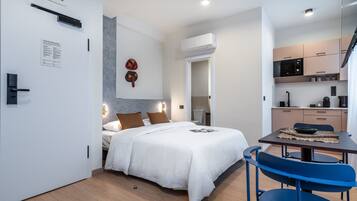 A modern hotel room with a bed, a small kitchenette, and a dining area.
