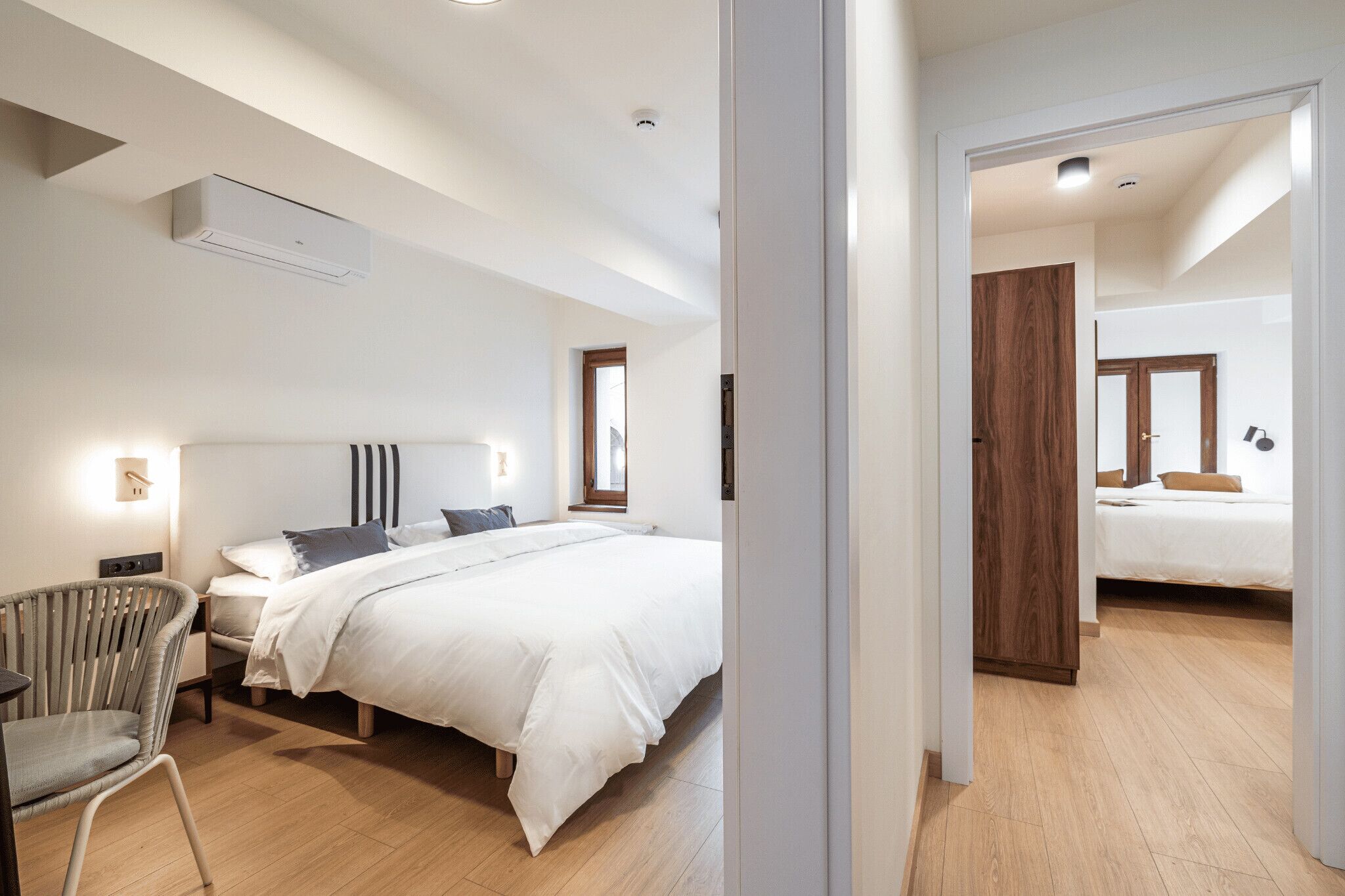 A modern bedroom with a large bed, bedside tables, a chair, and a wardrobe.