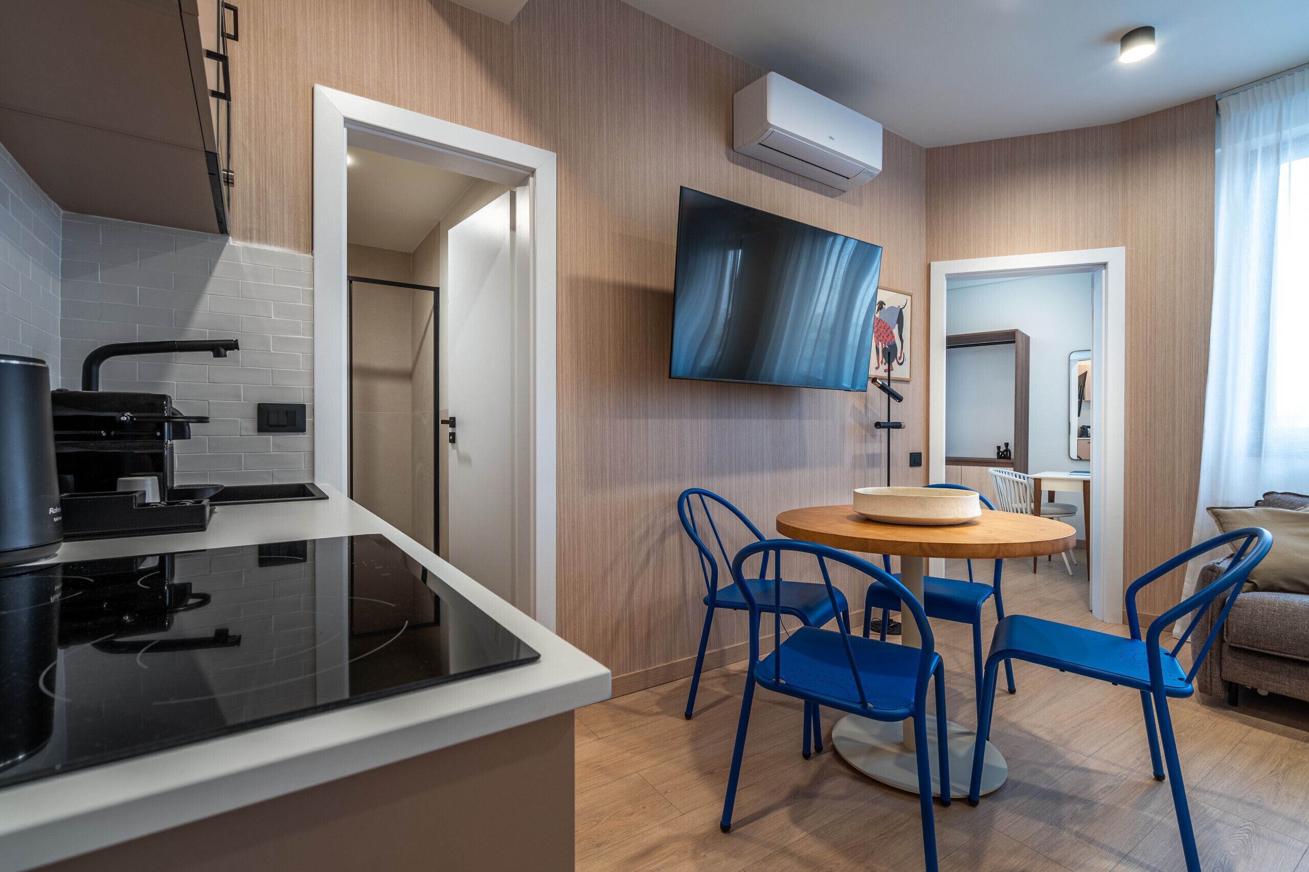 Una cocina moderna con estufa negra, un comedor con sillas azules y un televisor de pantalla plana montado en la pared.
