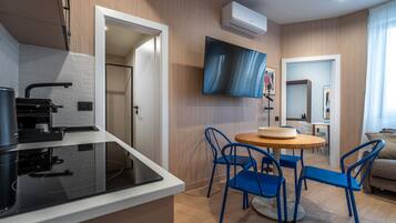 Una cocina moderna con estufa negra, un comedor con sillas azules y un televisor de pantalla plana montado en la pared.