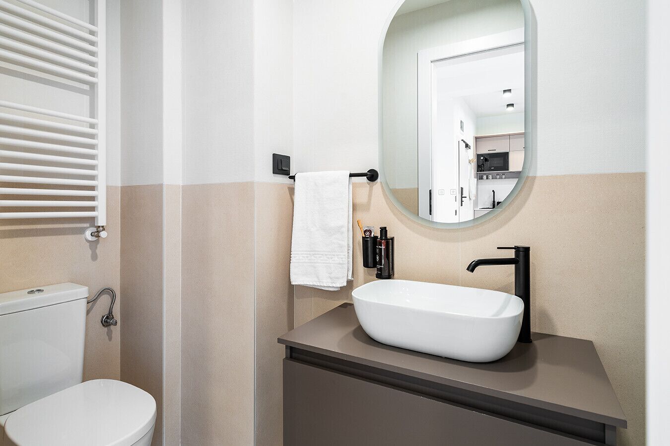 Een moderne badkamer met een wit toilet, een vrijstaand wastafelmeubel met een grote spiegel en een handdoekrek.