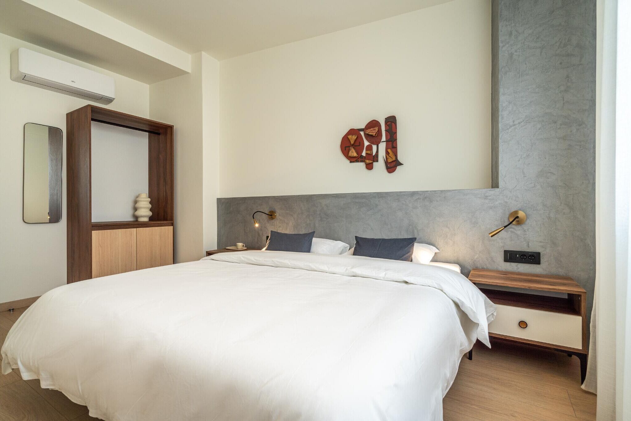 A modern bedroom with a large bed, bedside tables, a mirror, and a wall-mounted artwork.