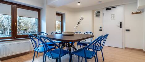 A dining area with a round table and blue chairs, a window with a view of buildings, and a white door with a sign.