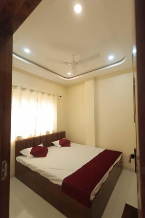 A bedroom with a bed, curtains, a ceiling fan, and a light fixture. - Hotel Ujjain Dwarka Palace (Ujjain)