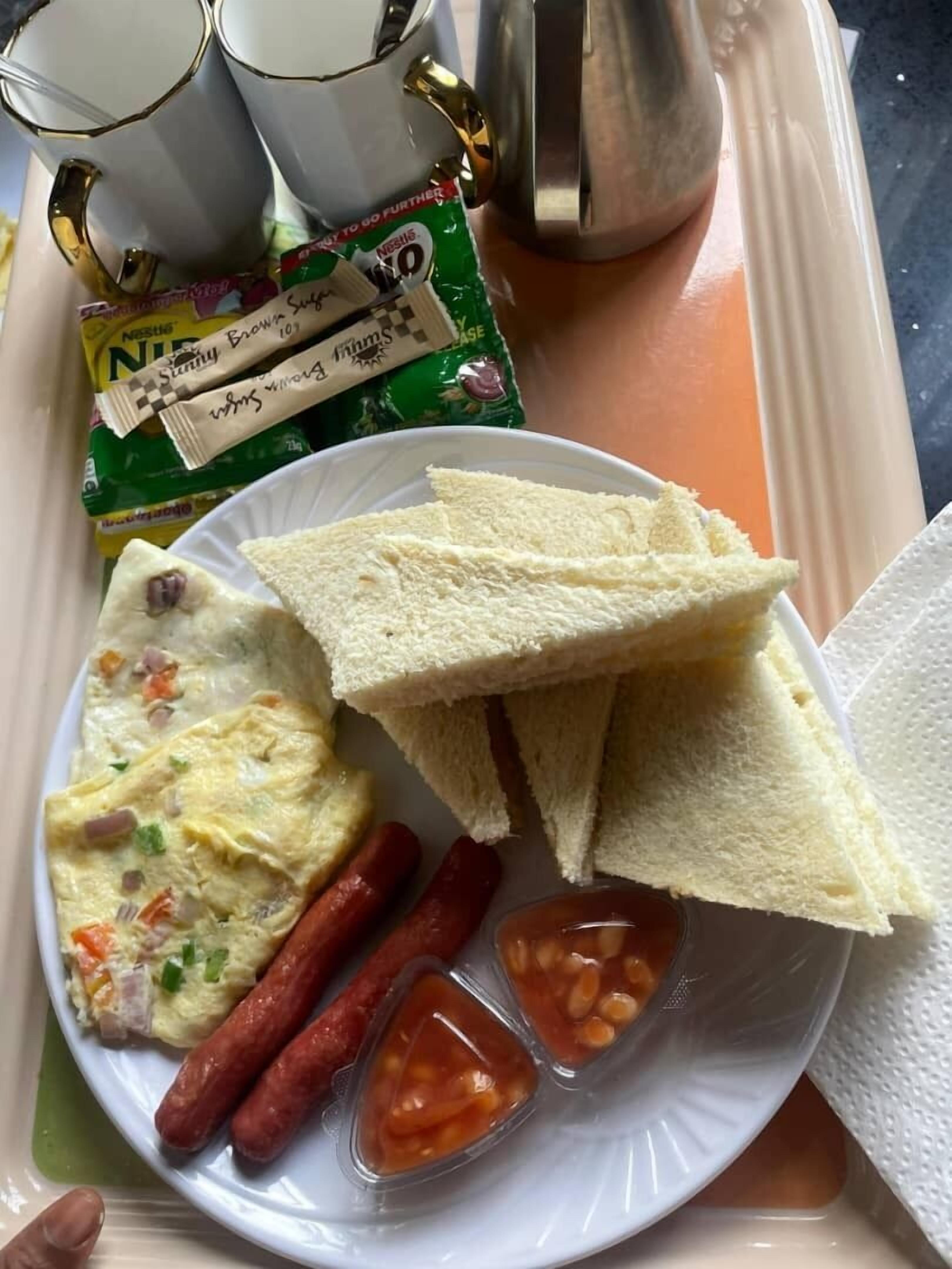 Un plato con tostadas, salchichas y un plato de huevos revueltos, acompañado de salsas y un paquete de café.