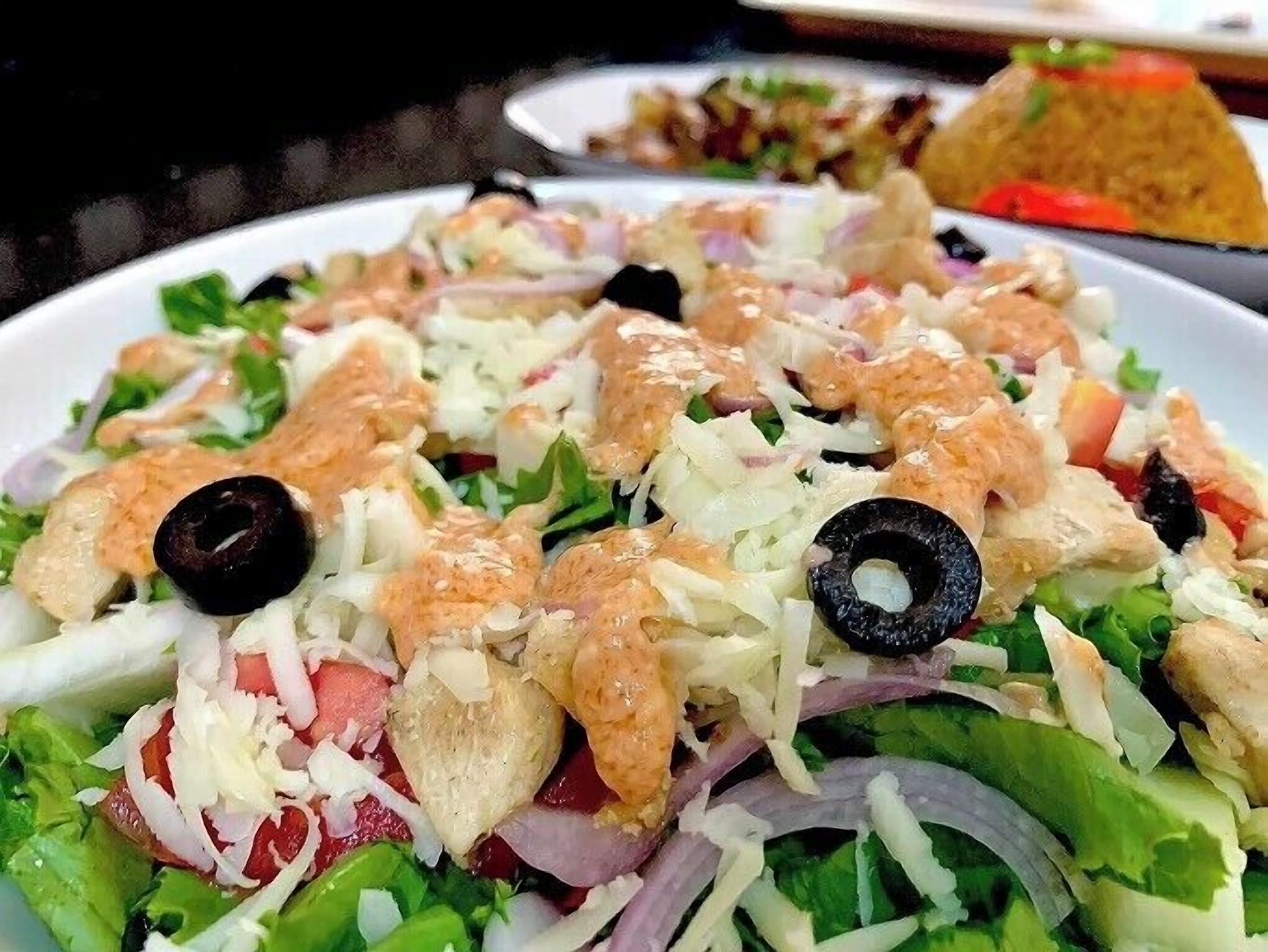 A plate of salad with lettuce, tomatoes, onions, black olives, and chicken pieces.