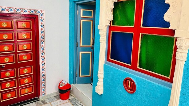 A room with a blue wall, a red door, and a window with a decorative frame. -  Connecting you with the Heritage & History of Udaipur. (Udaipur)