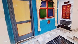 A room with a blue wall, a yellow door, and a red door with decorative elements. -  Connecting you with the Heritage & History of Udaipur. (Udaipur)