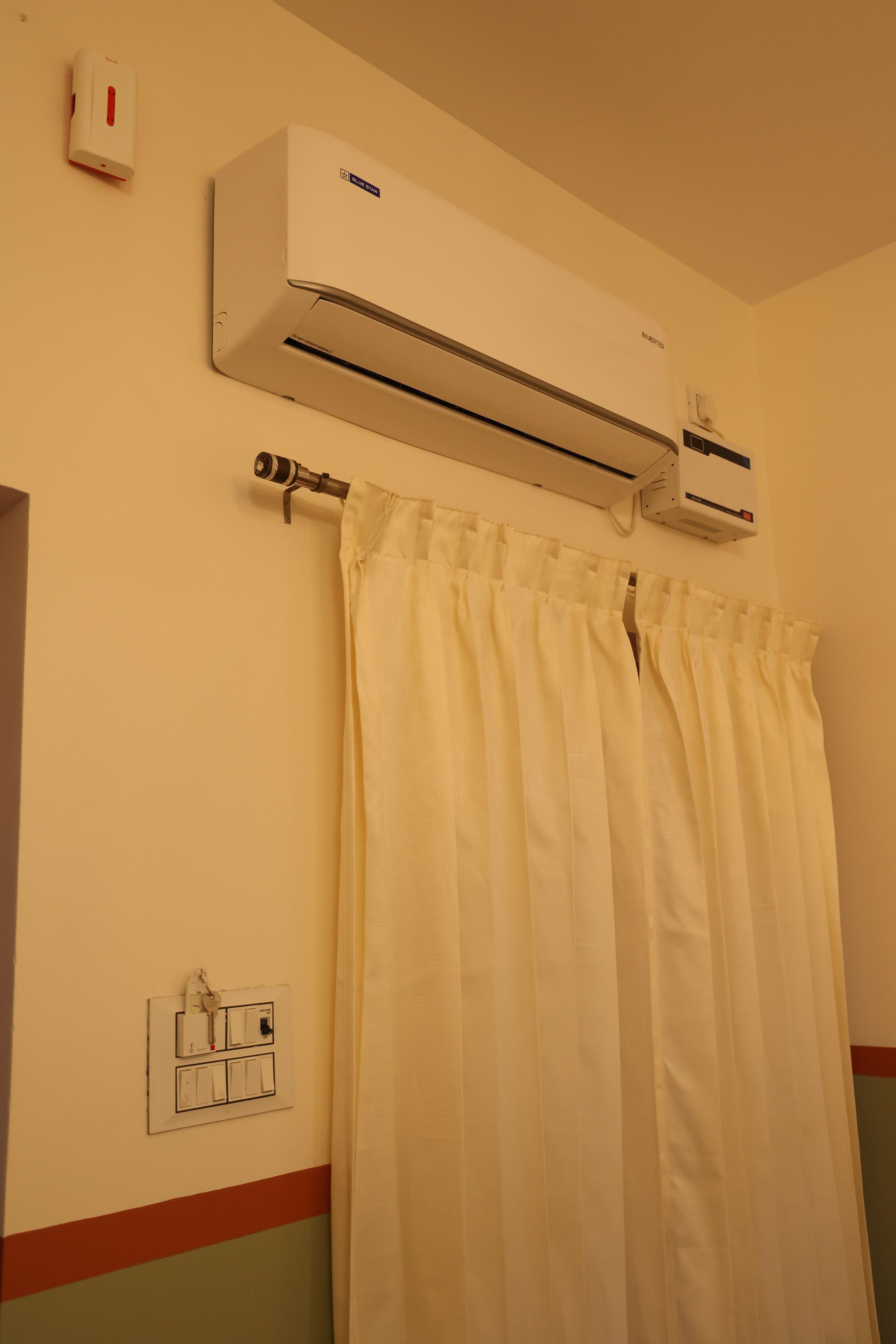 A bathroom with a white shower curtain, an air conditioning unit mounted on the wall, and a wall-mounted light switch.