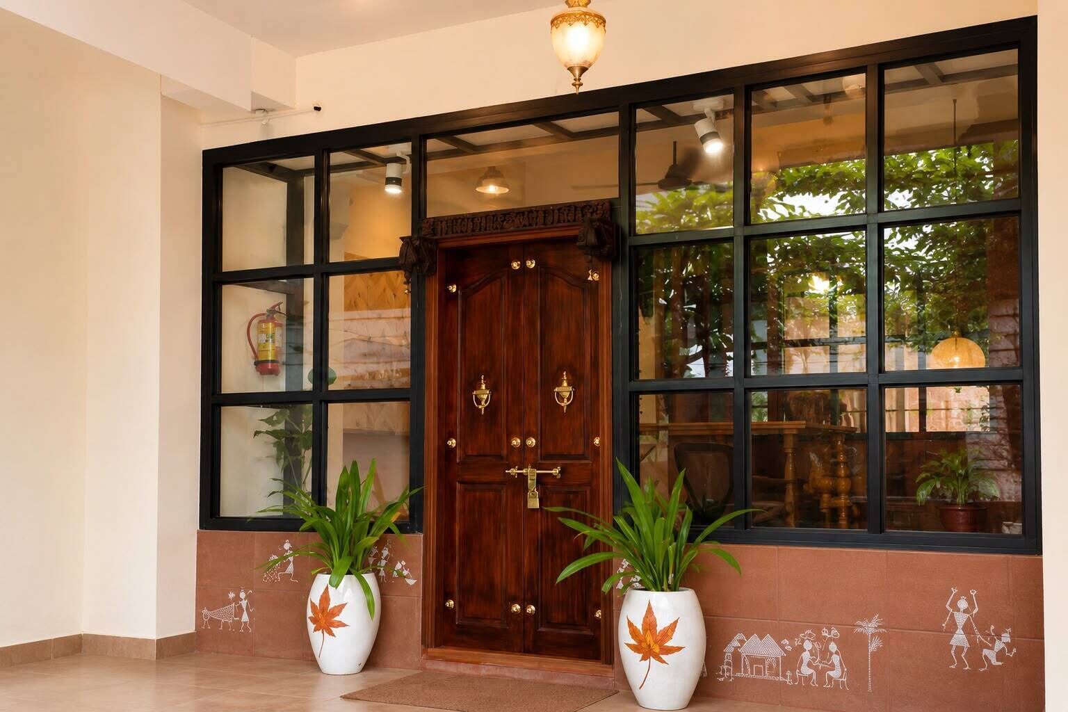 A hotel entrance with a large wooden door, two potted plants, and a view of greenery through the windows.
