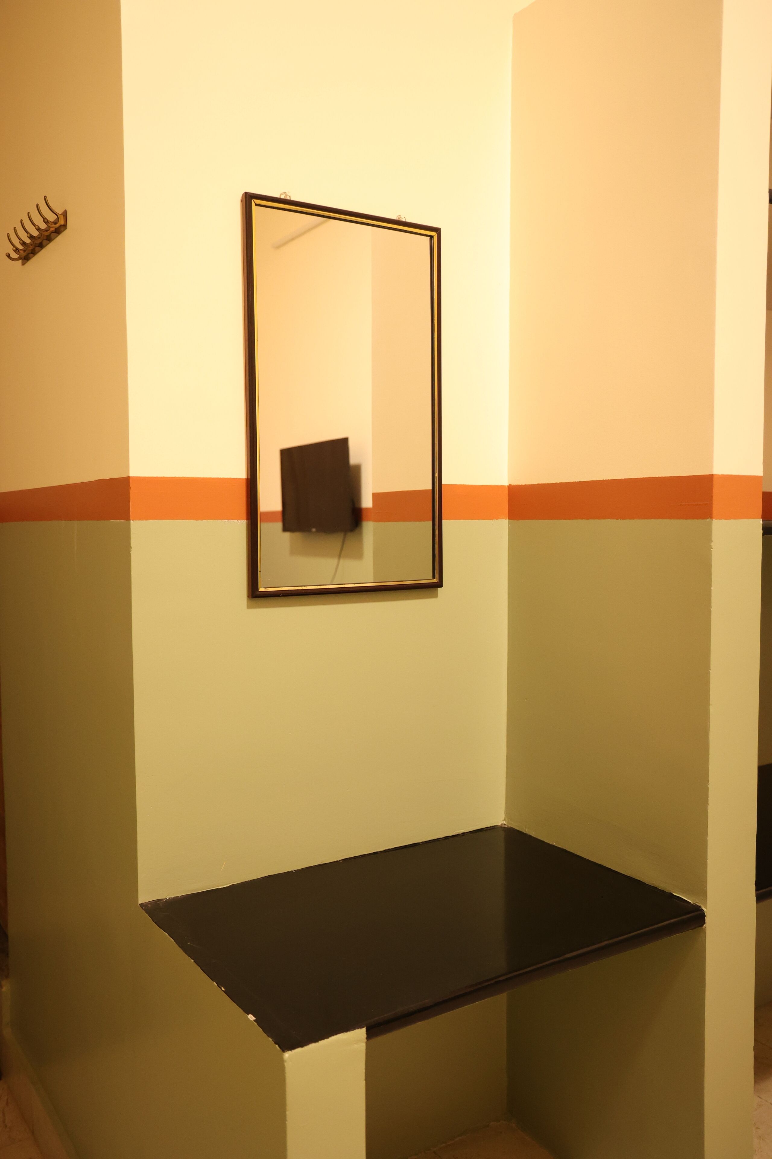 Un rincón de habitación con un banco negro, un espejo en la pared y un perchero.