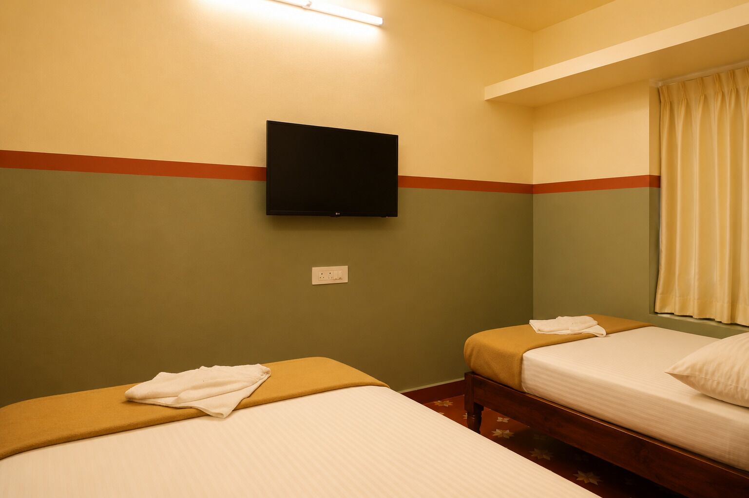 Une chambre d’hôtel avec deux lits, un téléviseur à écran plat fixé au mur et une fenêtre avec des rideaux.