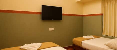 Une chambre d’hôtel avec deux lits, un téléviseur à écran plat fixé au mur et une fenêtre avec des rideaux.