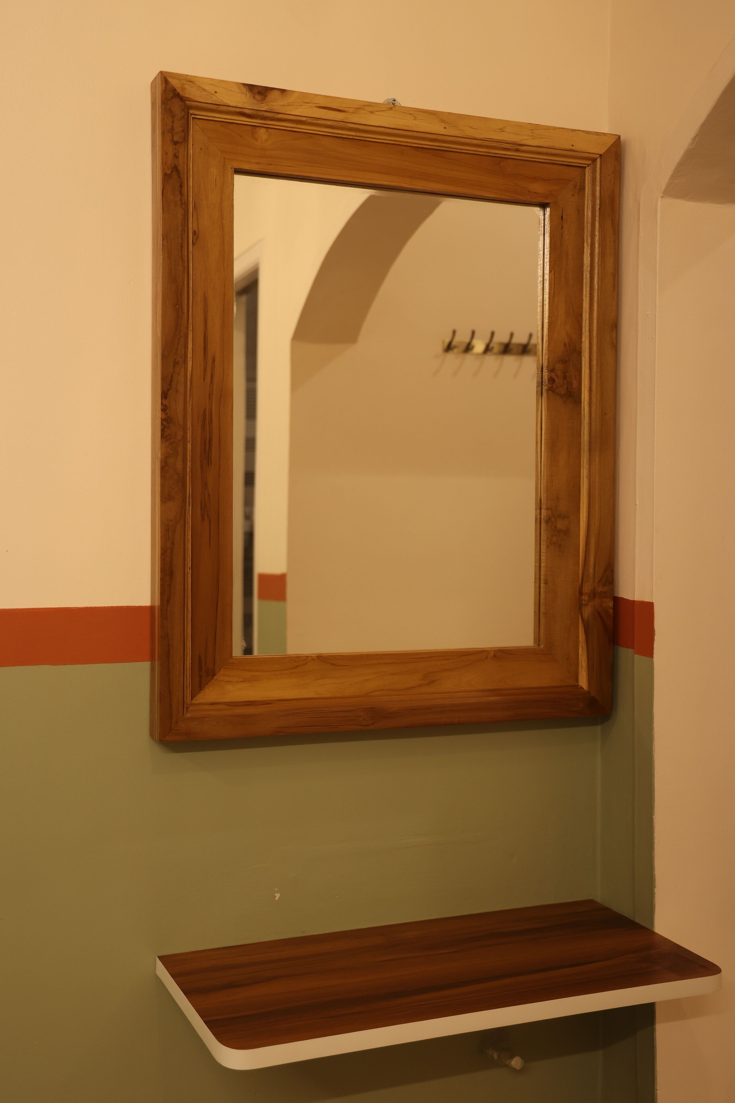 A wooden-framed mirror with a wooden shelf below it.