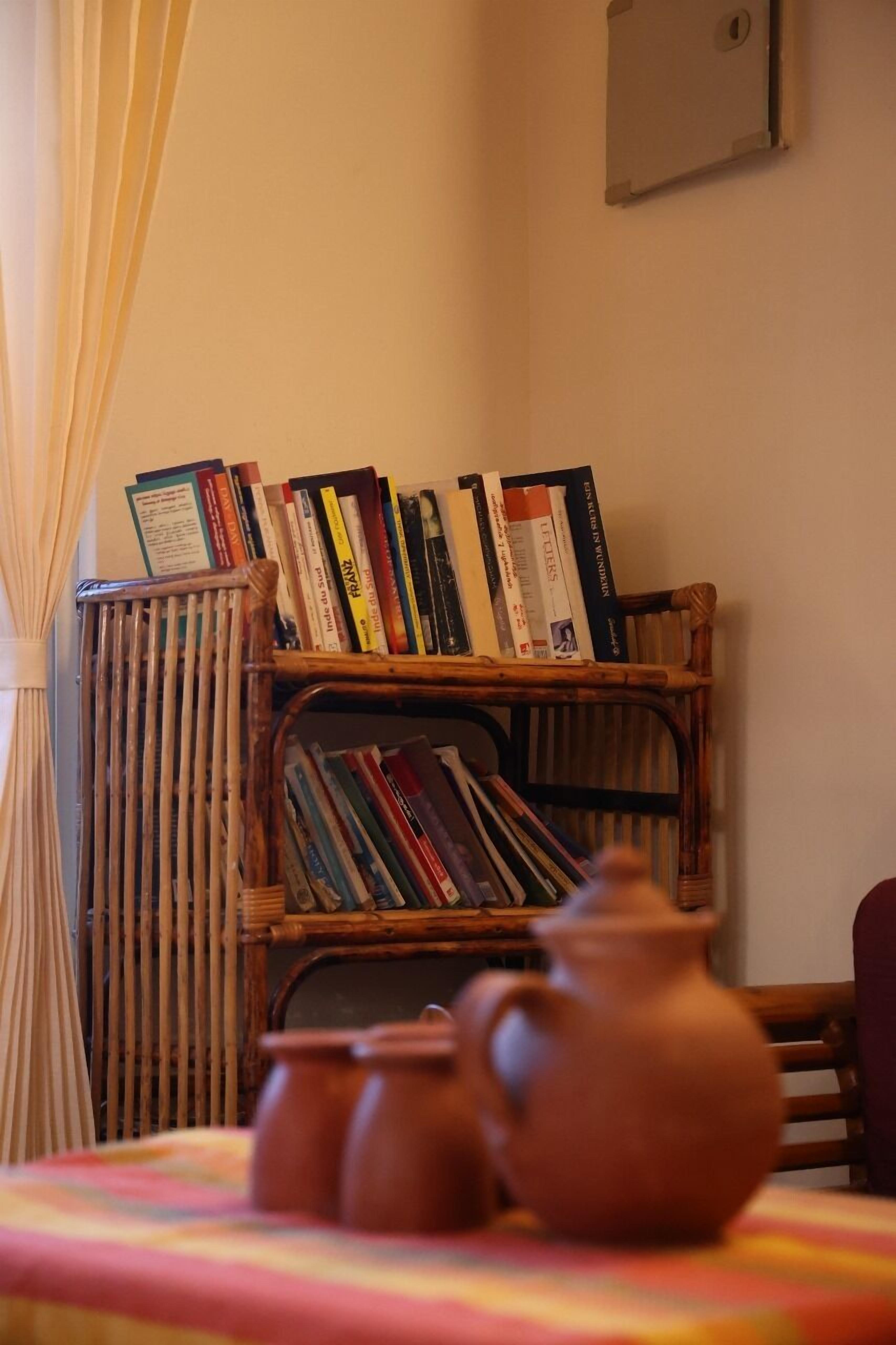 Een kamer met een boekenplank vol boeken, een tafel met een terracotta pot en een radiator.