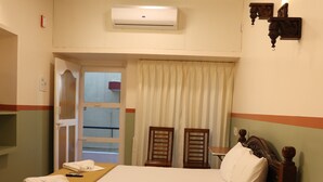 Ein ordentlich bezogenes Bett mit Holz-Kopfseitenverkleidung, einem Nachttisch, einem Deckenventilator und einer Klimaanlage an der Wand.