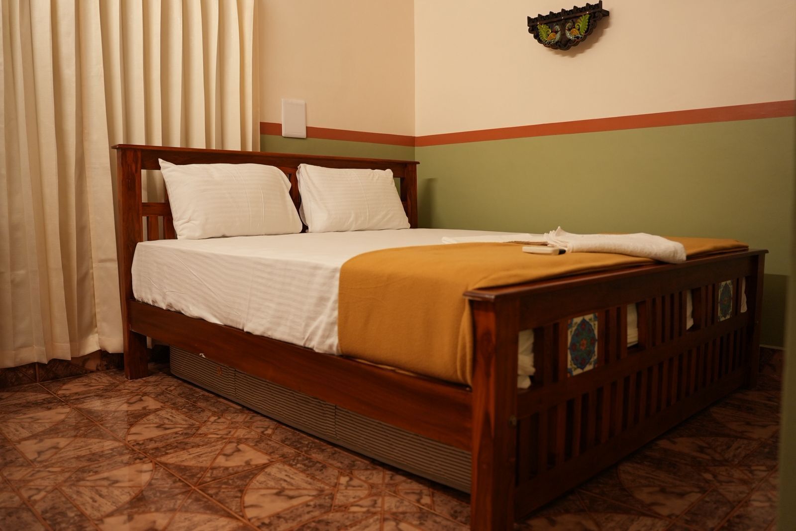 A single bed with a wooden frame and white bedding, a wall-mounted light fixture, and a window with curtains.
