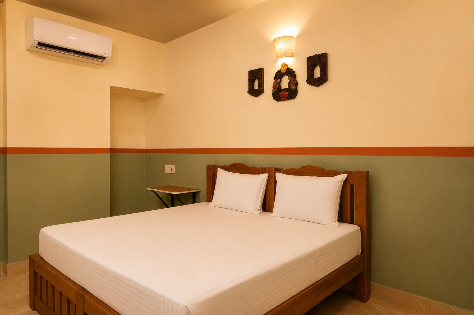 A hotel room with a bed, a nightstand, an air conditioning unit, and wall-mounted light fixtures.