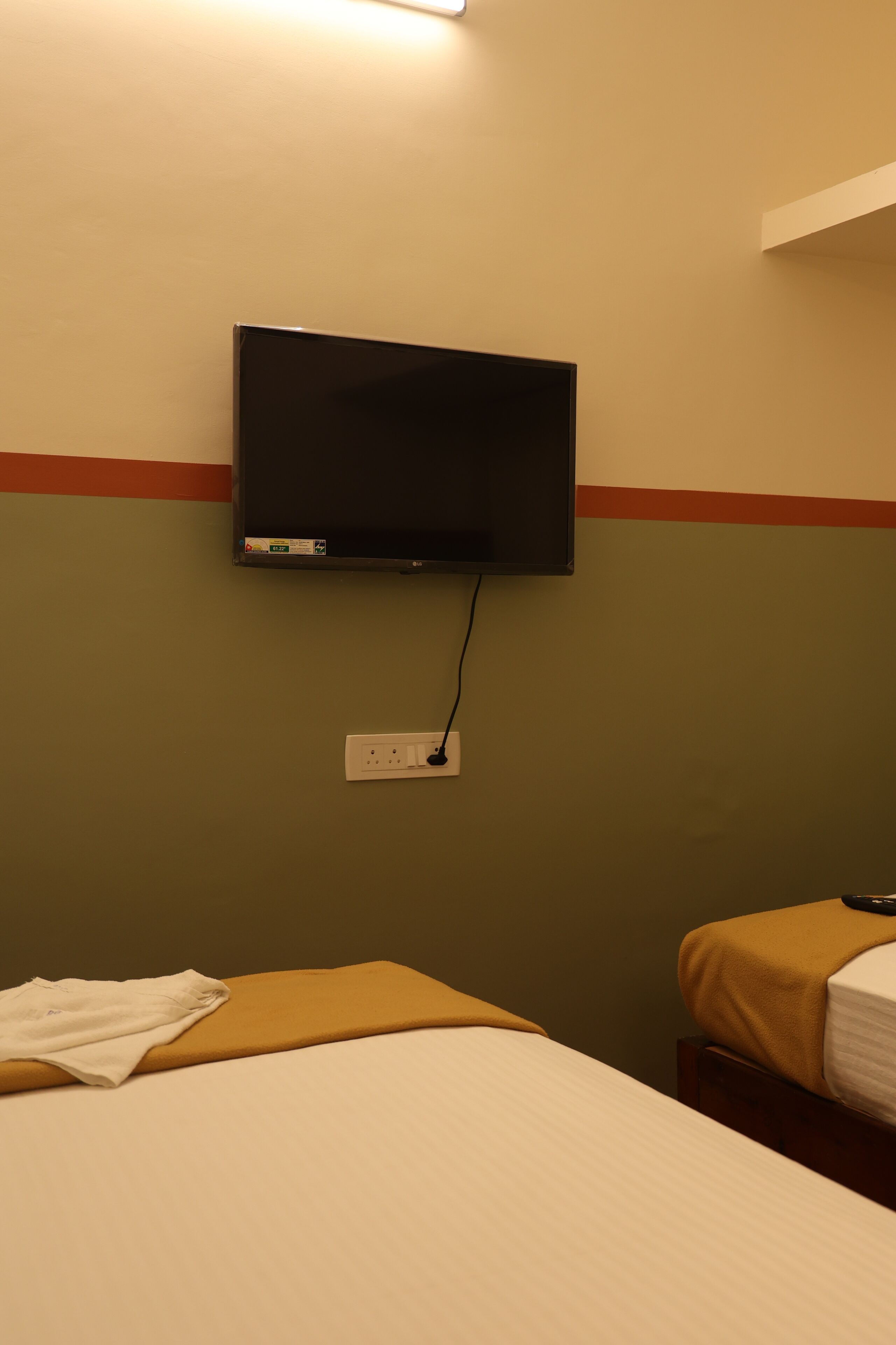 Ein Hotelzimmer mit an der Wand montiertem Fernseher, einem Bett mit weißer Bettdecke und einem Nachttisch mit Fernbedienung.