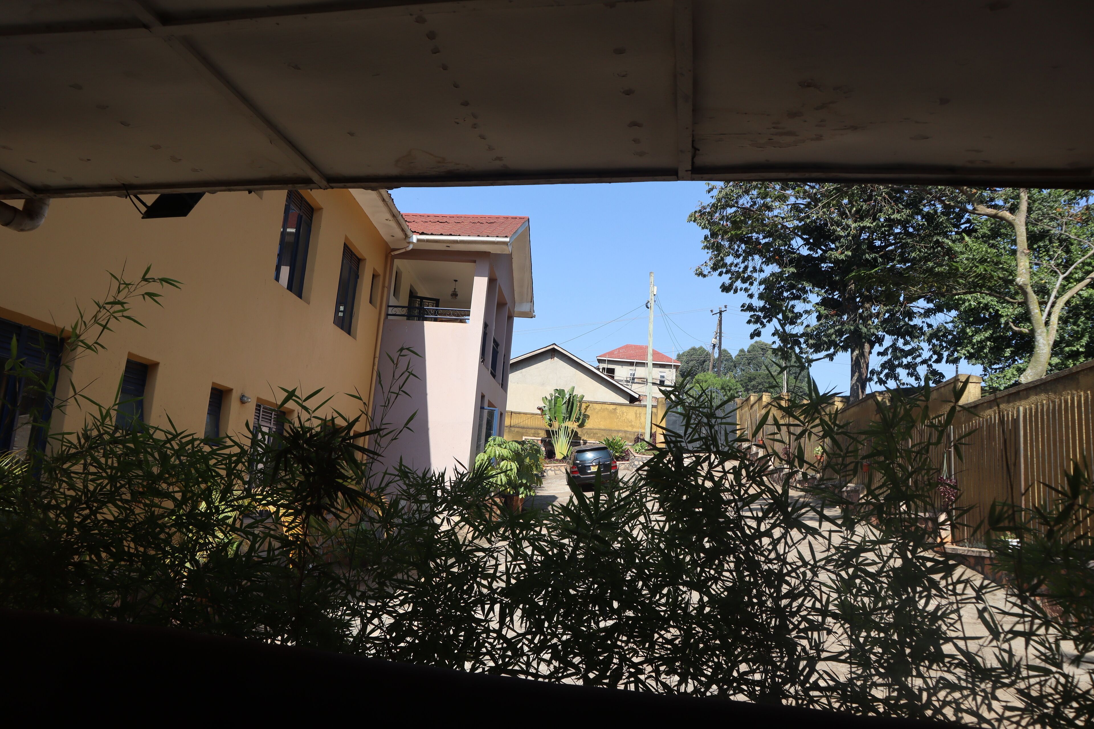Un quartier résidentiel avec une maison à deux étages, une voiture garée devant, et une rue bordée d’arbres et d’une clôture.