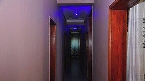 Un couloir étroit, avec des portes en bois de chaque côté et un plafond éclairé d’une lumière bleue.